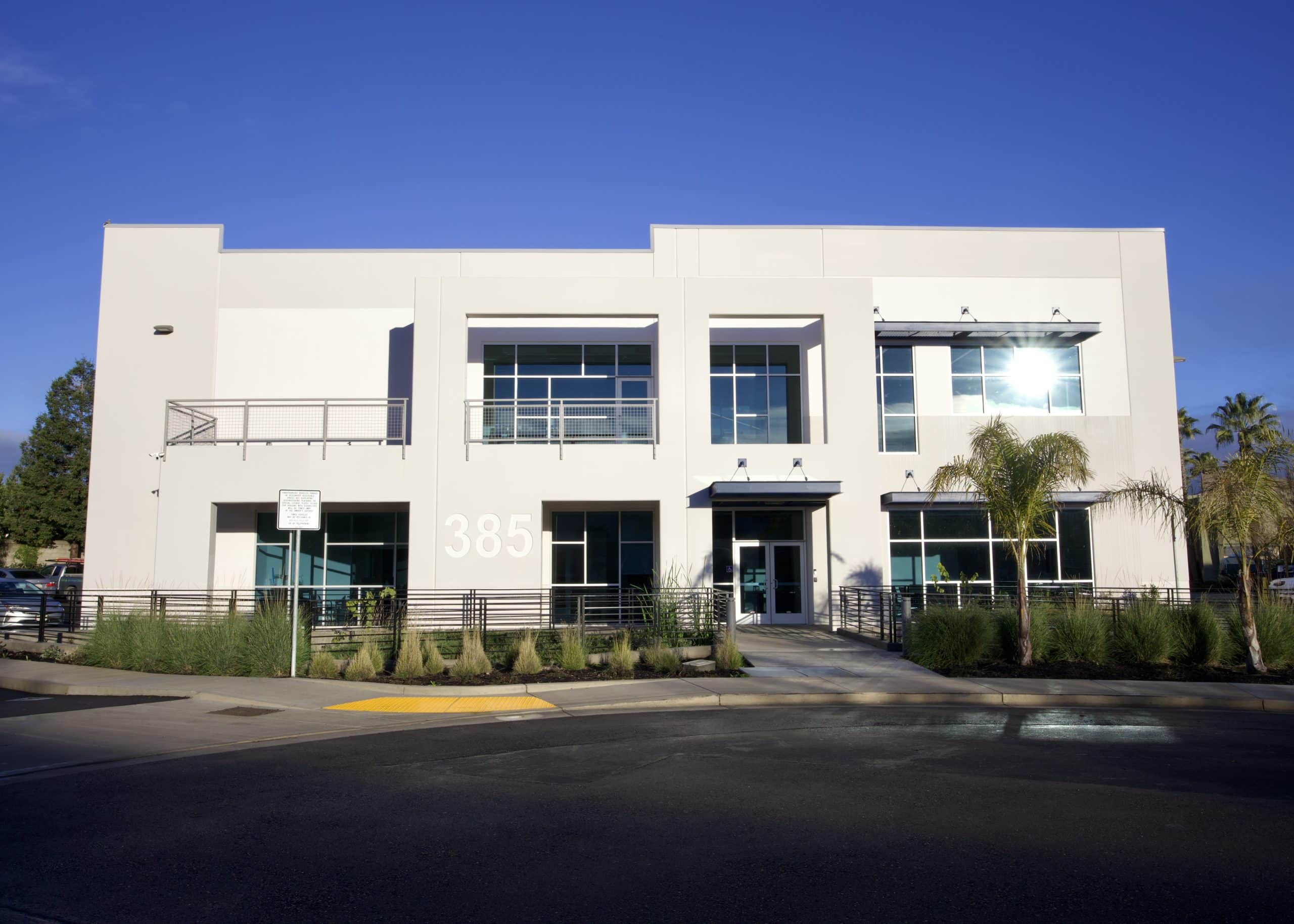 Two-story modern office building with large windows, palm trees, and the number 385.
