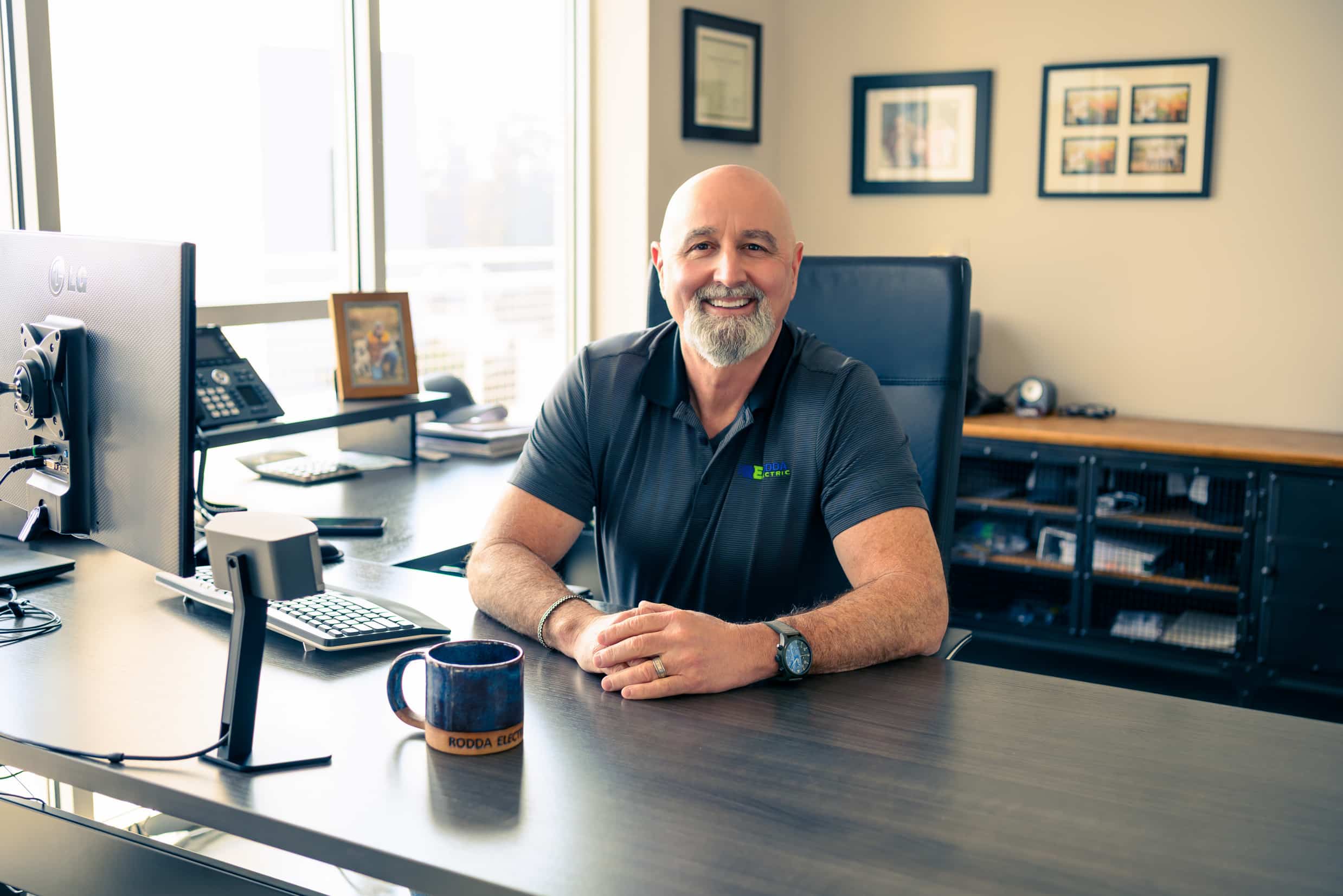 Smiling man sitting at a modern office desk with a computer and coffee mug.
