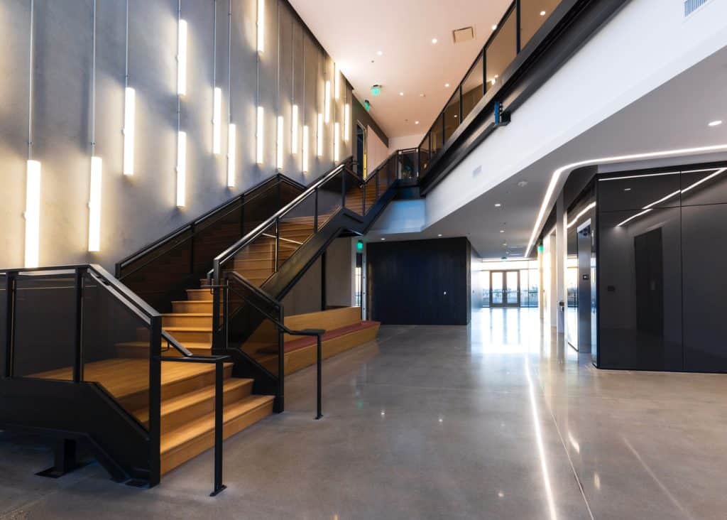 Modern interior with wooden stairs, hanging lights, and polished concrete floors.