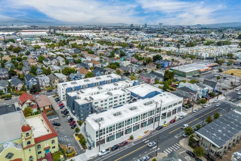 Aerial view of a city neighborhood with houses, streets, and industrial buildings in the distance.