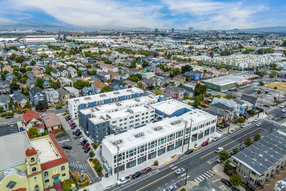 Aerial view of a city neighborhood with houses, streets, and industrial buildings in the distance.