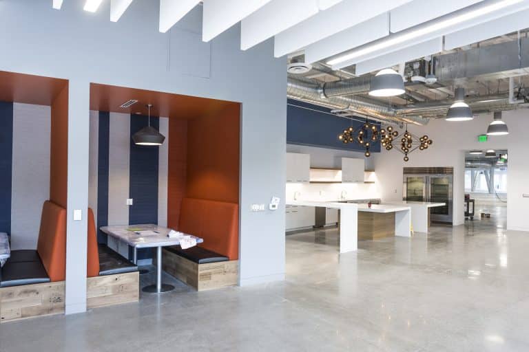 Modern office kitchen with booth seating, pendant lights, and polished concrete floors.