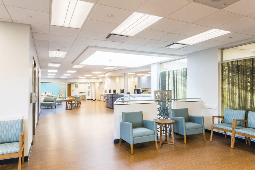 Bright, modern hospital waiting area with blue chairs, wood flooring, and large windows.