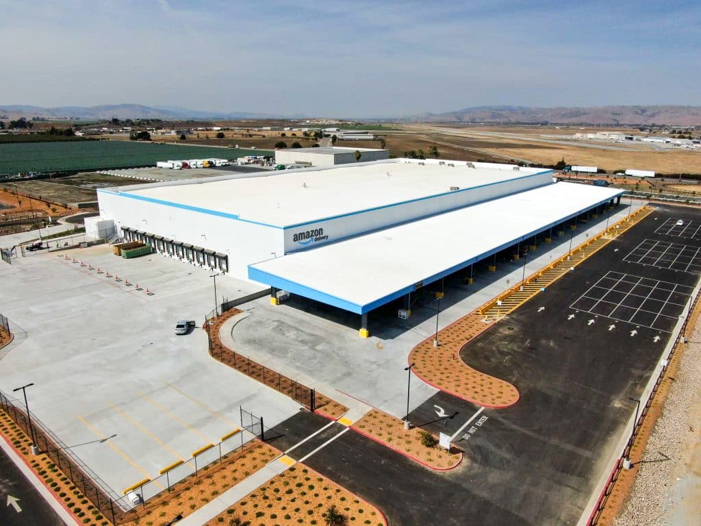 A large Amazon warehouse with loading docks and an adjacent mostly empty parking lot.