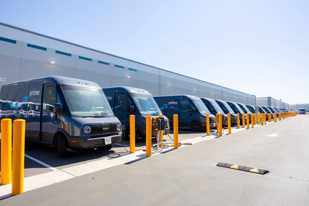 A row of Amazon Prime delivery vans parked at a warehouse charging station.