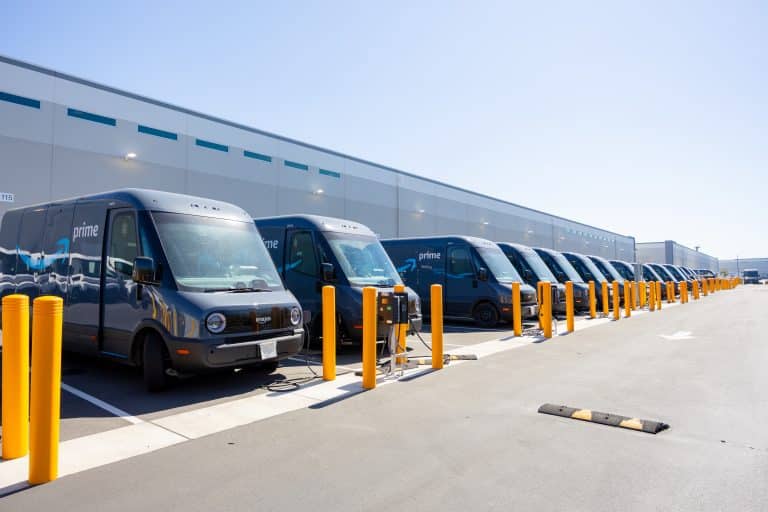 A row of Amazon Prime delivery vans parked at a warehouse charging station.