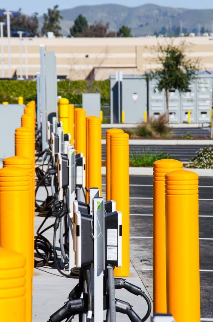 A row of electric vehicle charging stations with bright yellow protective posts.