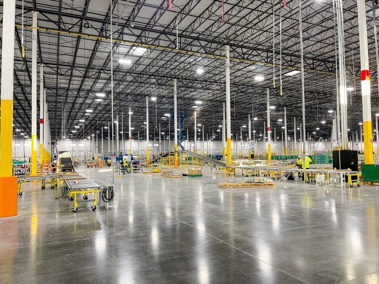 Large, brightly lit warehouse with conveyor belts, shelves, and empty open floor space.