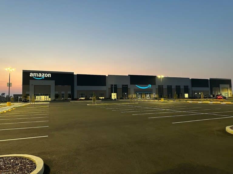 Amazon warehouse building at dusk with empty parking lot in the foreground.