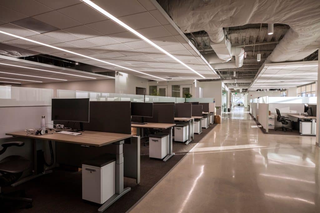 Modern, empty open-plan office with cubicles, desks, and overhead lighting.