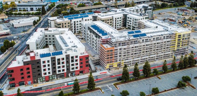 Aerial view of a large apartment complex under construction with solar panels on the roof.