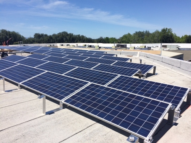 Rows of solar panels installed on a flat rooftop under a clear blue sky.