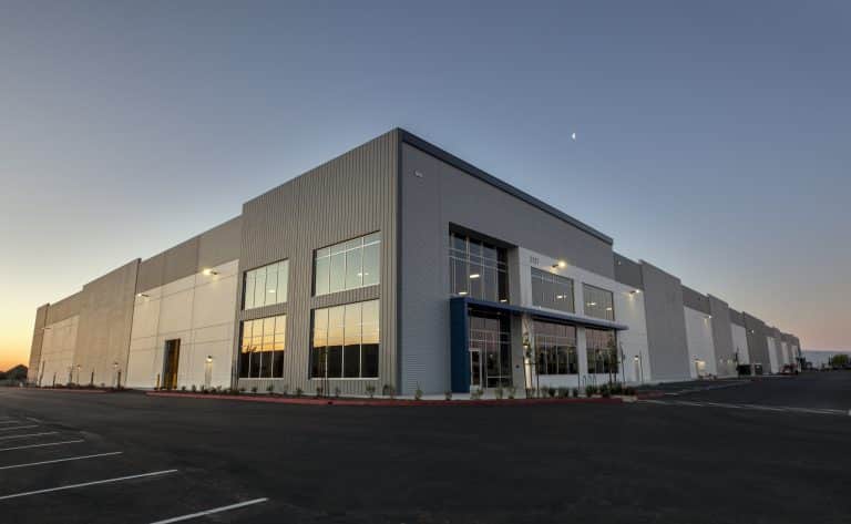 Large modern warehouse building at sunset with empty parking lot in front.