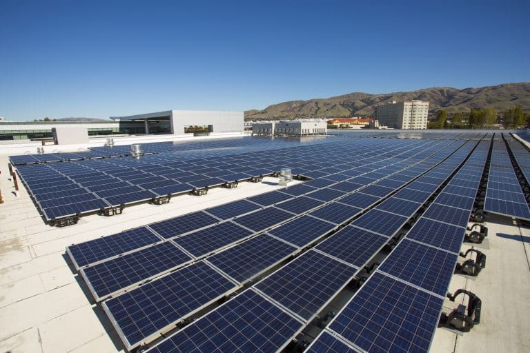 Rows of solar panels on a rooftop under a clear blue sky with mountains in the background.