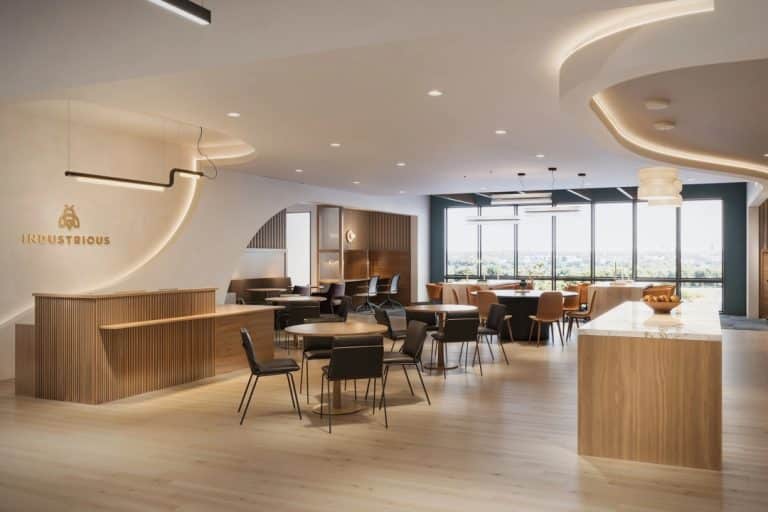 Modern office lounge with wood furniture, round tables, and large windows with a city view.