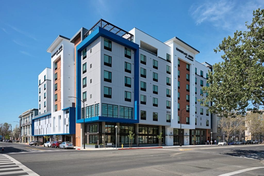 Modern mid-rise apartment building on a sunny day at a street corner with parked cars.