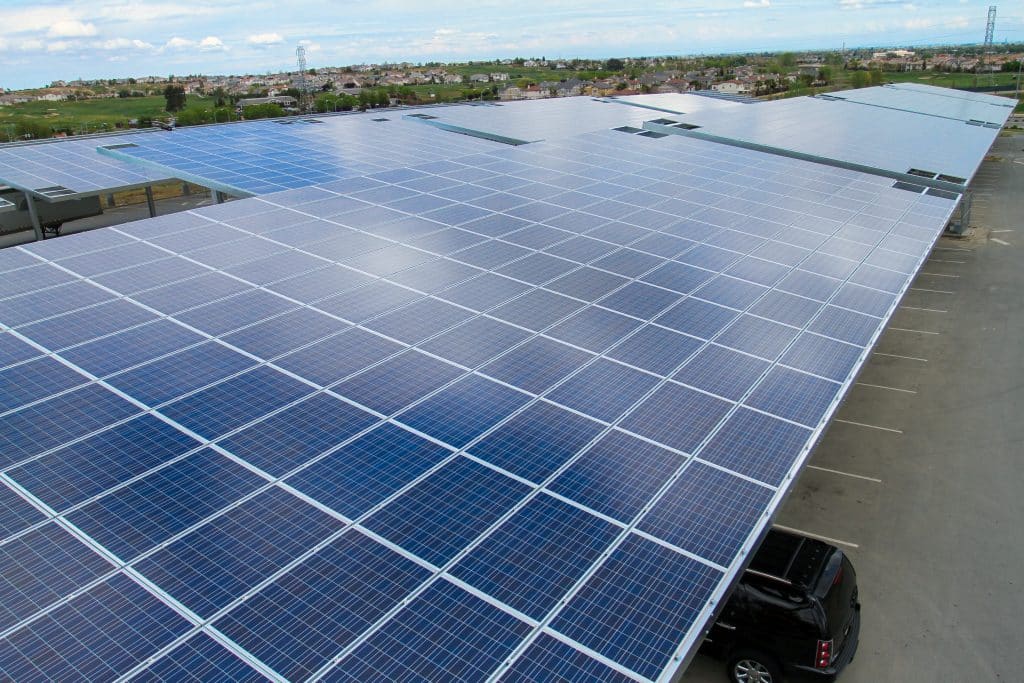 Large array of solar panels installed on a rooftop over a parking lot under a blue sky.