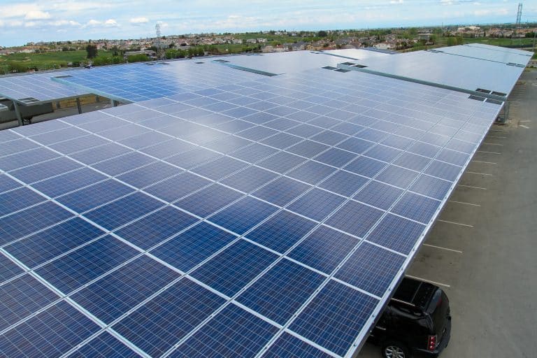 Large array of solar panels installed on a rooftop over a parking lot under a blue sky.