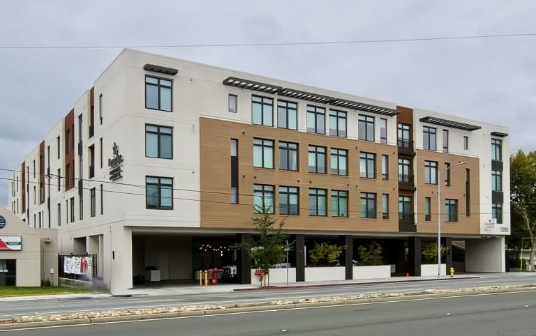 Modern four-story apartment building with large windows and brown and white exterior accents.