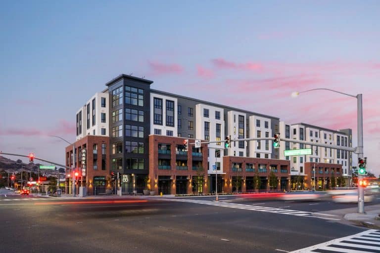 Modern, multi-story apartment building at a busy intersection during sunset.