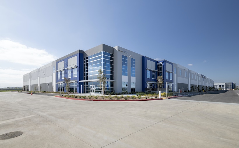 Modern industrial warehouse with large glass windows and a spacious, empty parking lot.
