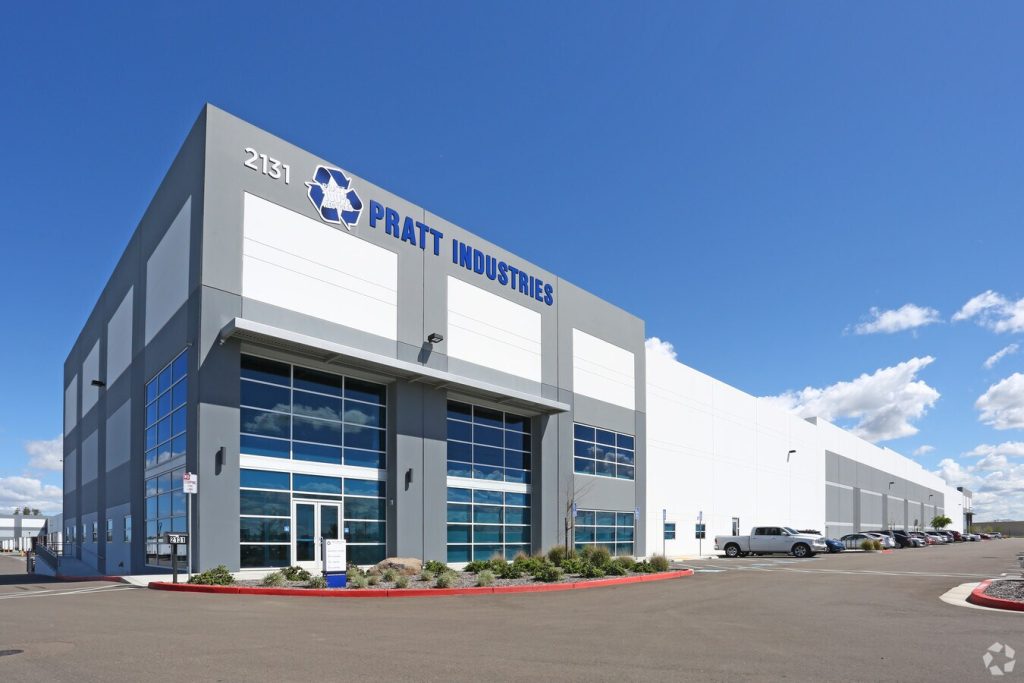 Large modern warehouse building with Pratt Industries sign and parked cars outside.