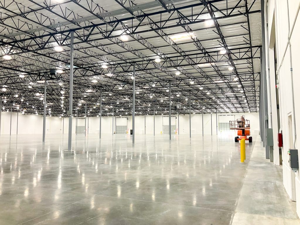 Spacious, empty warehouse interior with high ceilings, polished floors, and steel pillars.