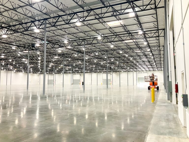 Spacious, empty warehouse interior with high ceilings, polished floors, and steel pillars.