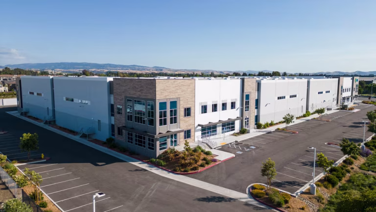Modern industrial warehouse building with large parking lot on a clear sunny day.