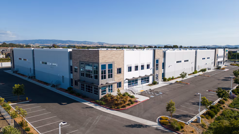 Modern industrial warehouse building with large parking lot on a clear sunny day.