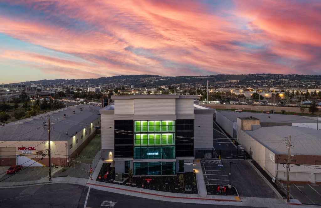 Modern building with green-lit windows under a vibrant pink and blue sunset sky.