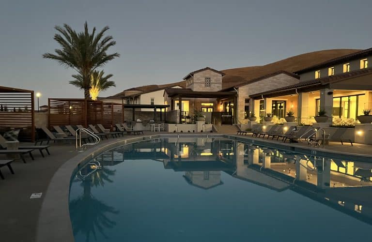 Outdoor pool with lounge chairs, palm tree, and modern building at dusk.