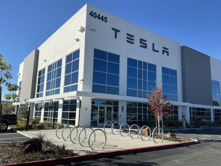 Modern Tesla office building with large windows, bike racks, and clear blue sky above.