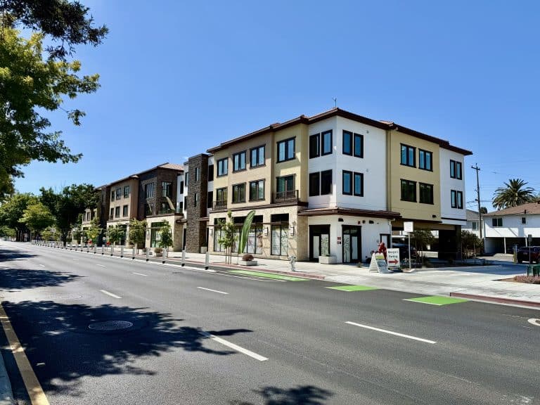 Modern three-story apartment building along an empty street on a sunny day.
